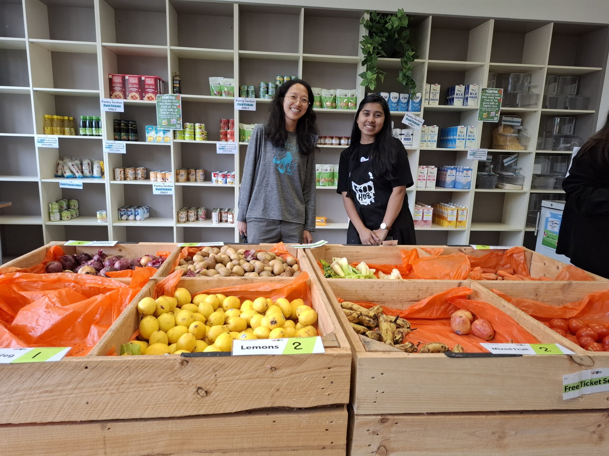 Two ladies stand behind a large crate of fruit and vegetables