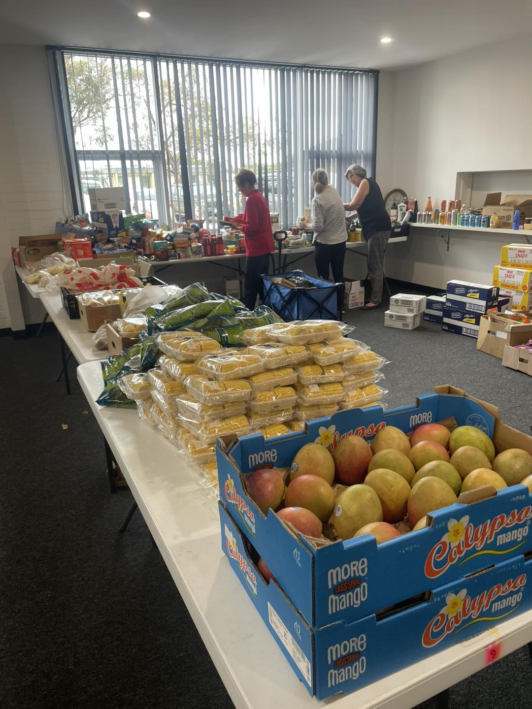 mangoes, corn and various other fruit and vegetables sit in crates on trestle tables.